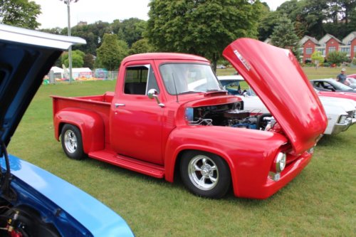 The front side of a classic Ford F100 Truck painted in bright red with the hood lifted up